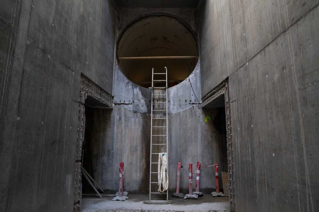 这张照片显示了一条大型直径隧道 - 正在建造的Kalvebod Brygge隧道项目。一个高的梯子向上延伸到隧道圆形开口的底部。梯子的底部位于一个具混凝土地板的区域，左侧和右侧是高高的混凝土墙。