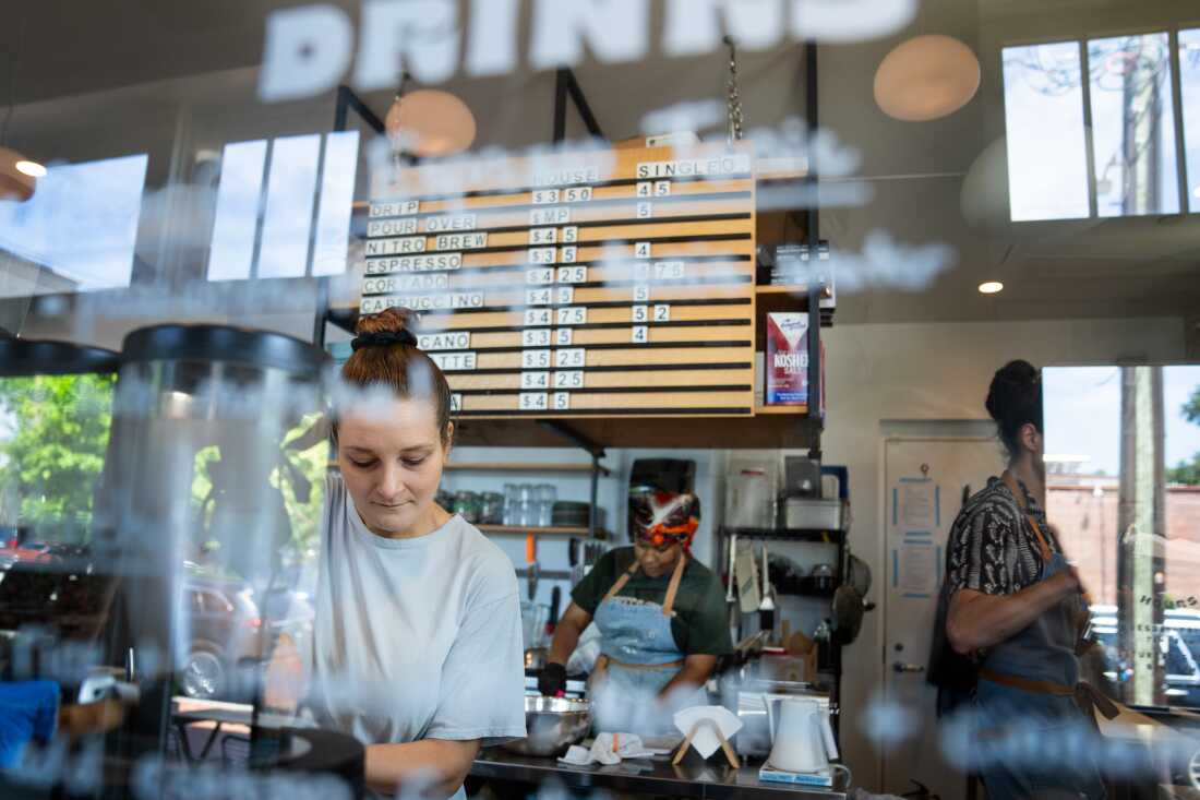 Kristen Tizaawie-Vogel在她后面的华盛顿特区的Takoma附近的Lost Sock Roasters'Coffee Shops饮料准备了一杯，有两名工人和一个菜单板显示价格。