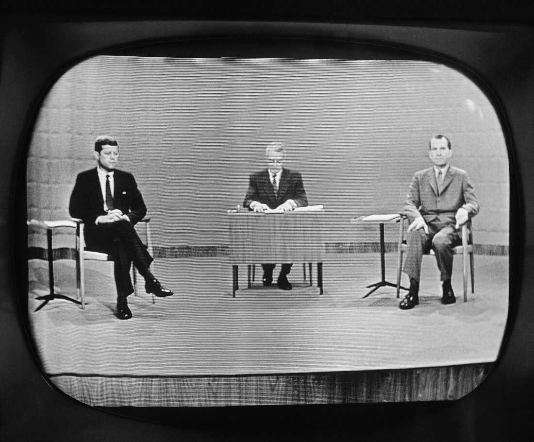 主持人霍华德·史密斯（Howard K. Smith）坐在参议员约翰·肯尼迪（John Kennedy）（左）和副总统理查德·尼克松（Richard Nixon）之间，他们在1960年9月26日在芝加哥的辩论中出现在电视工作室监视器上。