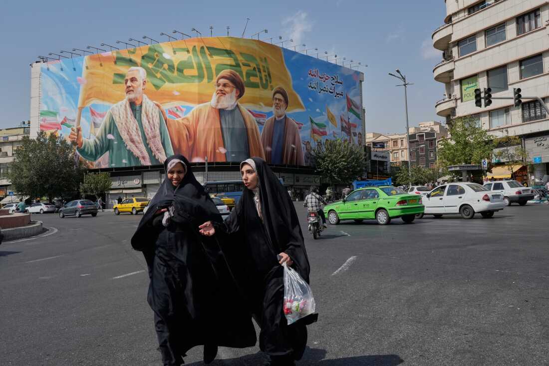 Two women walk past a huge banner showing the late commander of the Iran's Revolutionary Guard expeditionary Quds Force, Gen. Qassem Soleimani, who was killed in a US drone attack in 2020, and two late Hezbollah leaders Hassan Nasrallah, center, and Hashem Safieddine, who were killed in Israeli airstrikes in 2024, at the Enqelab-e-Eslami (Islamic Revolution) Square，2025年9月27日，星期六，在伊朗的德黑兰。