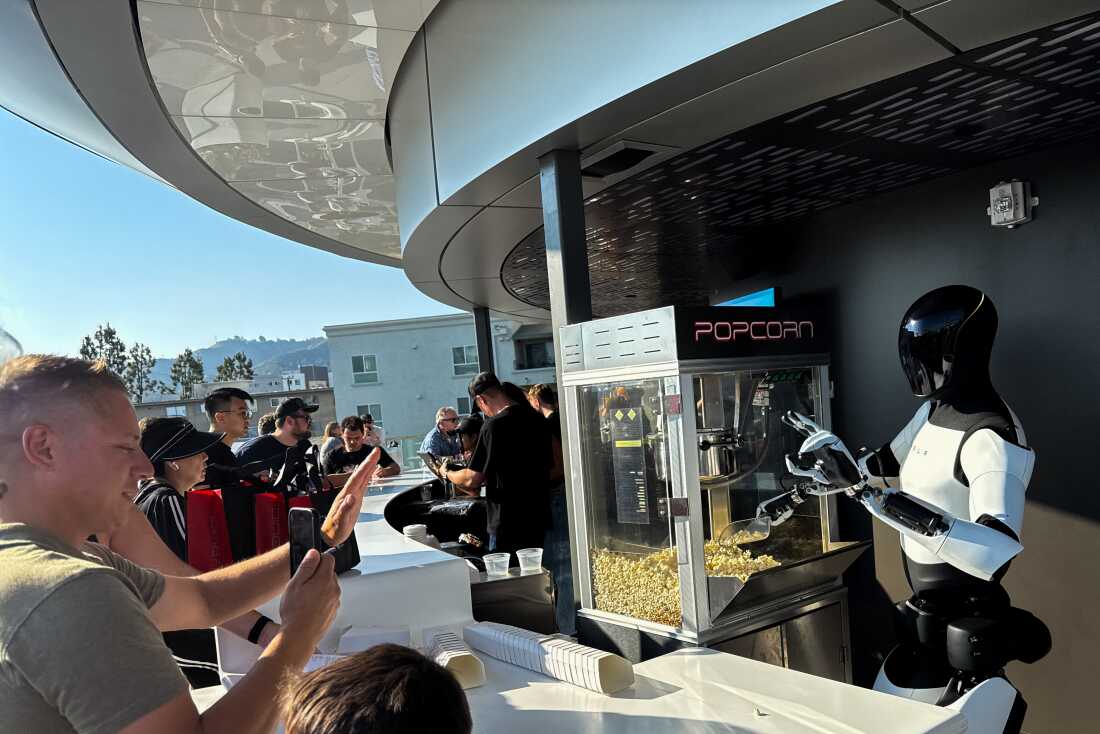 2025 年 7 月 21 日，在加利福尼亚州洛杉矶的 Tesla Diner、Drive-In 餐厅和 Supercharger 开业典礼上，特斯拉 Optimus 机器人舀起爆米花，并向与会者做出手势。