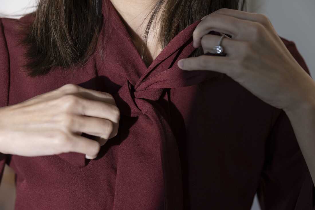 帕特尔身穿酒红色连衣裙，在脖子上系着蝴蝶结时双手的特写。