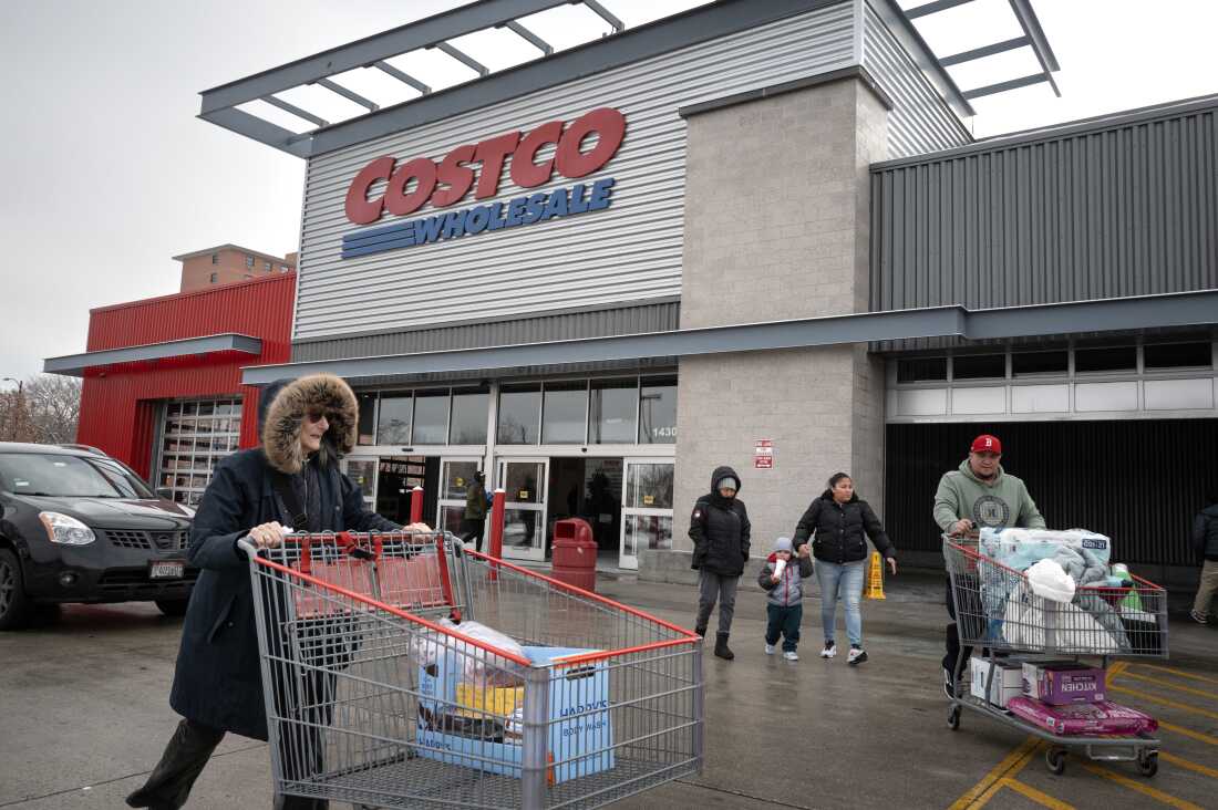 2025 年 12 月 2 日，顾客走在芝加哥 Costco 商店外的停车场。两人推着大型购物车。